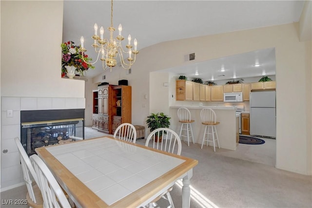 dining area featuring light colored carpet, visible vents, lofted ceiling, a tile fireplace, and a notable chandelier