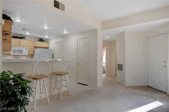 kitchen with visible vents, light brown cabinets, white appliances, recessed lighting, and a breakfast bar area