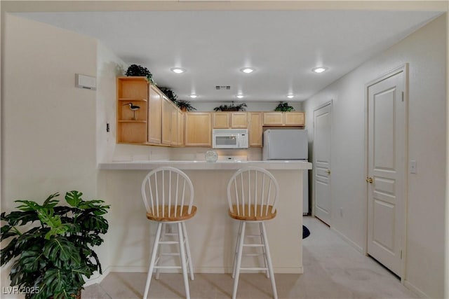 kitchen with white appliances, a peninsula, light brown cabinetry, open shelves, and light countertops