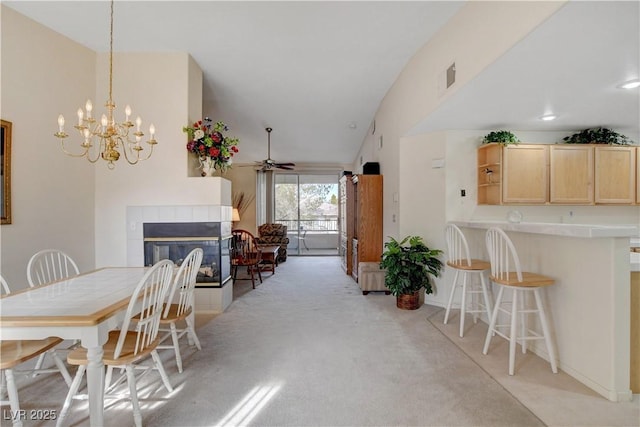 dining area with visible vents, a tiled fireplace, a ceiling fan, vaulted ceiling, and light colored carpet
