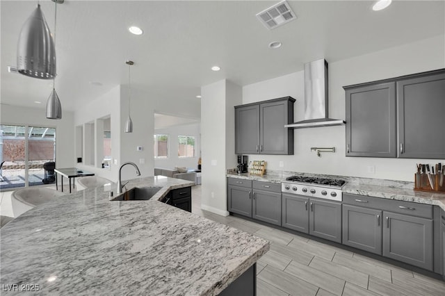kitchen featuring visible vents, a sink, wall chimney range hood, open floor plan, and stainless steel gas stovetop