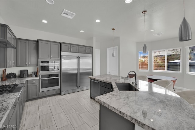 kitchen with light stone countertops, visible vents, appliances with stainless steel finishes, a sink, and gray cabinetry