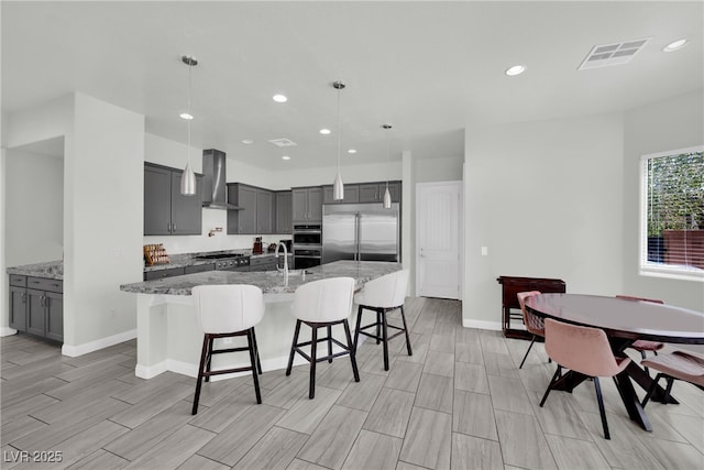 kitchen featuring gray cabinets, wall chimney range hood, visible vents, and stainless steel appliances