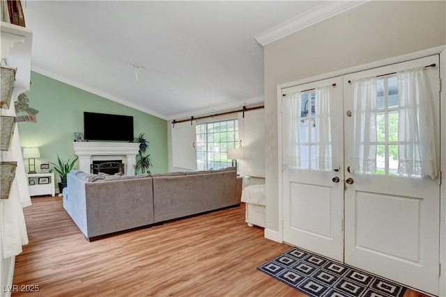 foyer featuring a fireplace, crown molding, light wood finished floors, french doors, and lofted ceiling