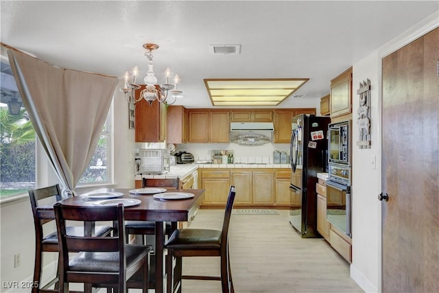 kitchen with range hood, visible vents, freestanding refrigerator, wall oven, and tile countertops