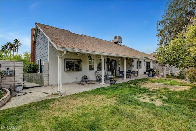 back of house featuring a shingled roof, a lawn, a chimney, a patio, and stucco siding
