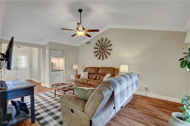 living room featuring visible vents, ornamental molding, a ceiling fan, light wood finished floors, and vaulted ceiling