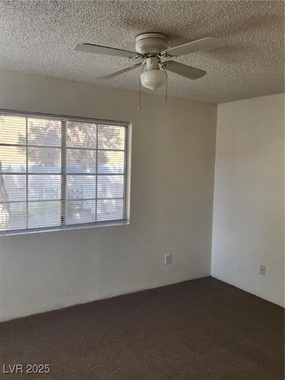 empty room with a textured ceiling, a ceiling fan, and dark carpet