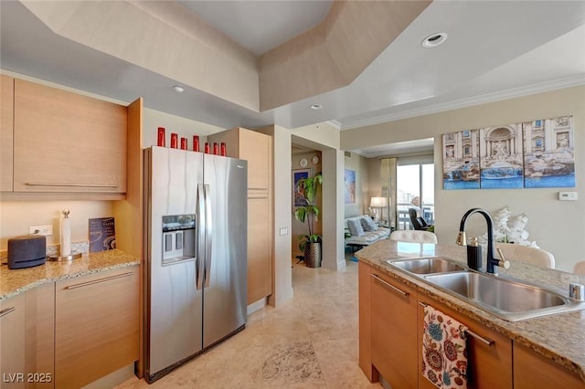 kitchen with stainless steel fridge, a sink, open floor plan, light stone counters, and ornamental molding