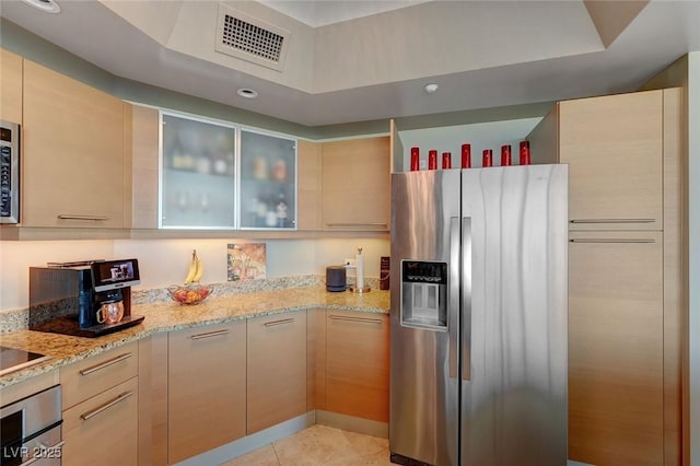 kitchen with visible vents, appliances with stainless steel finishes, glass insert cabinets, and light stone countertops