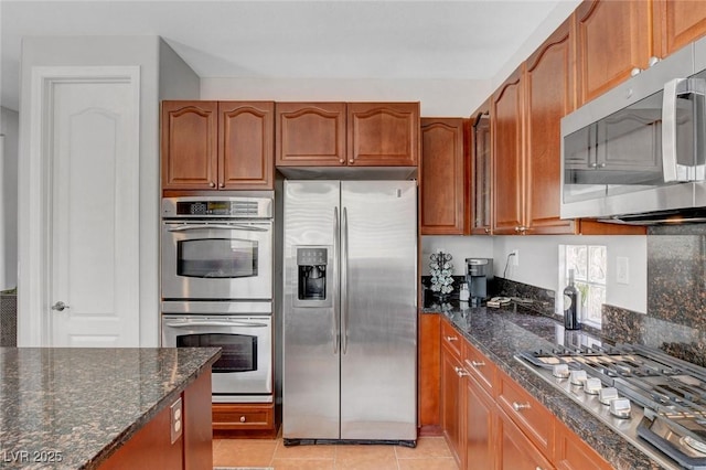 9413 Artesian Oak Ct, Las Vegas, NV 89149 - kitchen with stainless steel appliances, brown cabinets, dark stone countertops, and light tile patterned floors