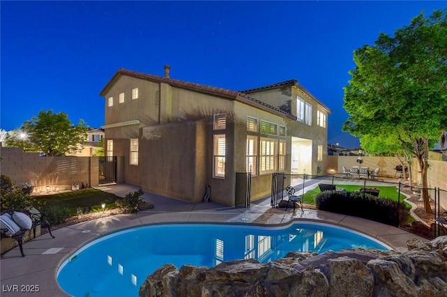 9413 Artesian Oak Ct, Las Vegas, NV 89149 - back of house at night featuring a fenced in pool, a patio area, a fenced backyard, and stucco siding