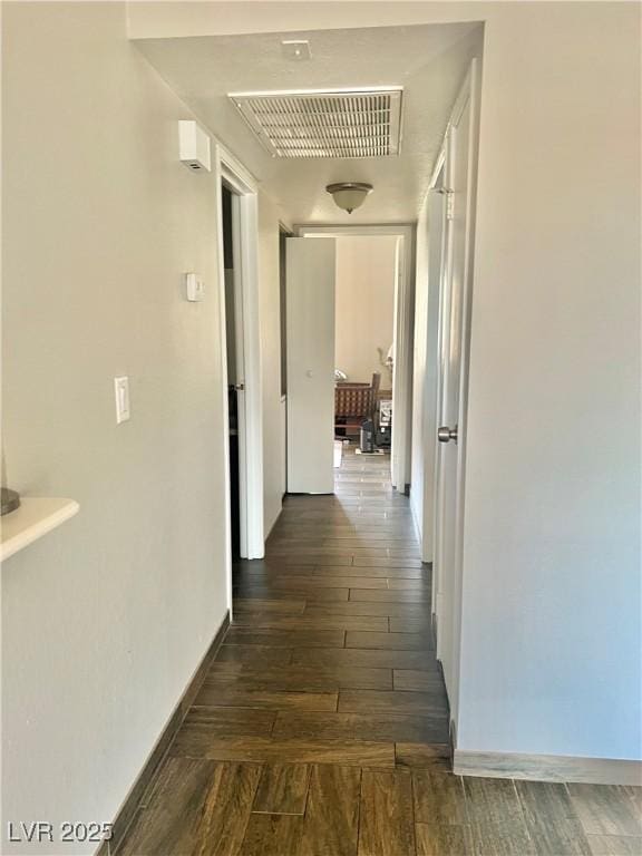 hall with visible vents, baseboards, and dark wood-style floors
