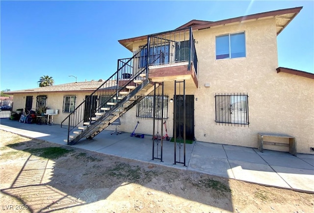 rear view of house featuring stairway, a patio, and stucco siding