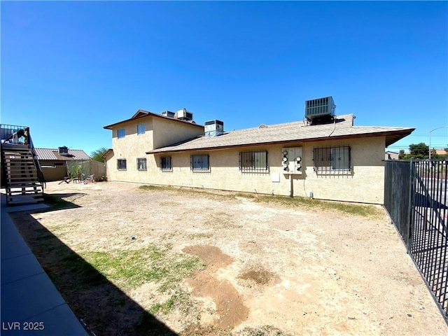 rear view of property featuring fence, central AC unit, and stucco siding