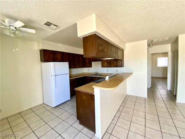 kitchen featuring a peninsula, light tile patterned floors, freestanding refrigerator, visible vents, and a sink