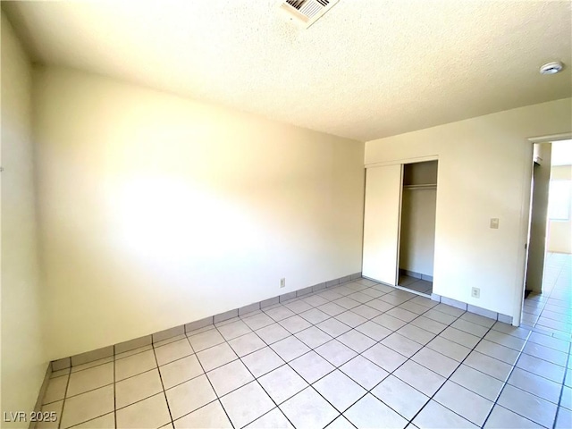 unfurnished bedroom featuring a textured ceiling, a closet, light tile patterned floors, and visible vents