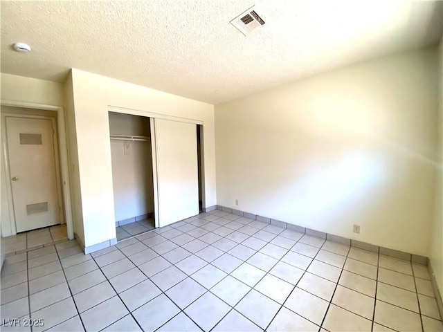 unfurnished bedroom featuring visible vents, a closet, a textured ceiling, and light tile patterned flooring