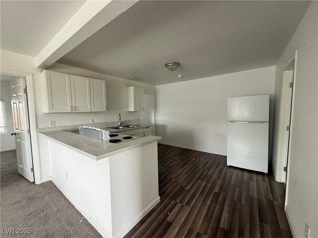 kitchen with dark wood-style floors, light countertops, freestanding refrigerator, white cabinetry, and a sink