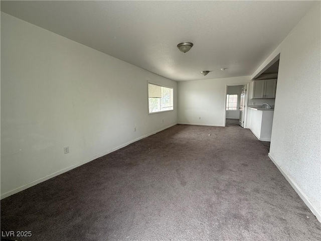 unfurnished living room with baseboards and dark colored carpet