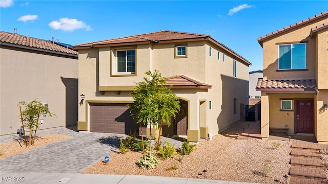 mediterranean / spanish-style house with a tile roof, stucco siding, an attached garage, and decorative driveway