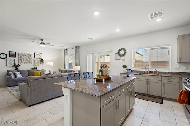 kitchen with gray cabinetry, a sink, a center island, a ceiling fan, and stone counters