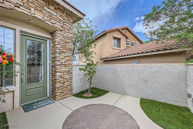 215 Sunset Shower Dr, Henderson, NV 89012 - view of exterior entry with a patio area, stone siding, a tiled roof, stucco siding, and fence