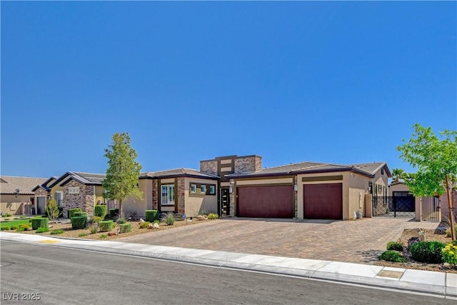 prairie-style home featuring stucco siding, a gate, decorative driveway, an attached garage, and fence