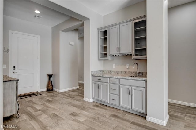 kitchen featuring baseboards, gray cabinetry, visible vents, light wood finished floors, and a sink