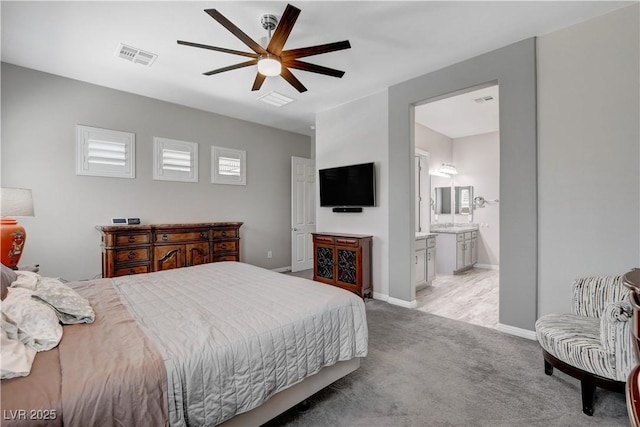 bedroom with baseboards, ensuite bathroom, a ceiling fan, visible vents, and light colored carpet