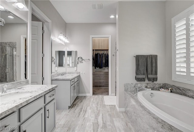 full bath featuring two vanities, a spacious closet, a shower stall, a bath, and a sink