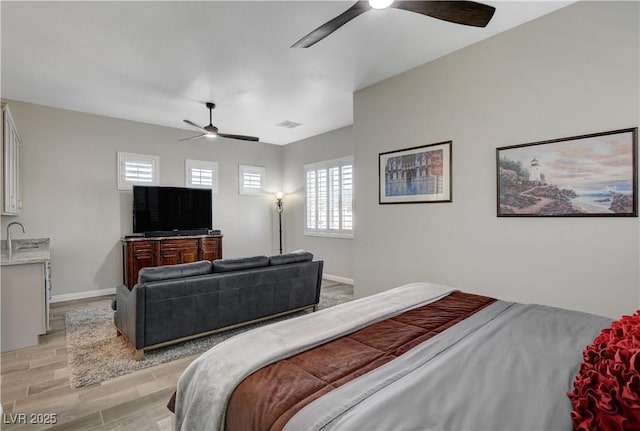 bedroom featuring baseboards, light wood-style flooring, visible vents, ceiling fan, and a sink