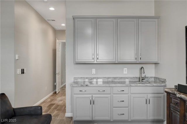 kitchen featuring visible vents, baseboards, a sink, light wood-style floors, and light stone countertops