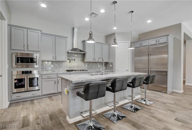 kitchen with built in appliances, visible vents, wall chimney exhaust hood, and gray cabinets