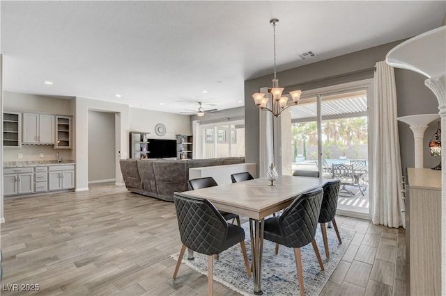 dining room featuring light wood-style floors, baseboards, visible vents, and ceiling fan with notable chandelier