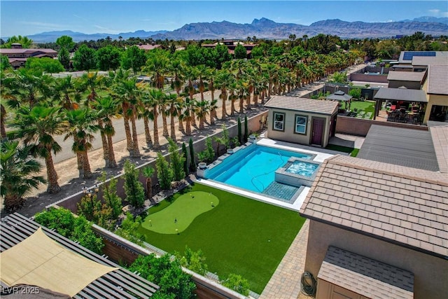 view of pool featuring a mountain view, a fenced backyard, a pool with connected hot tub, and an outbuilding