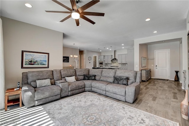 living area with light wood-type flooring, recessed lighting, and ceiling fan with notable chandelier
