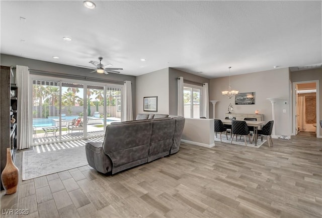 living area featuring recessed lighting, light wood-style floors, ceiling fan with notable chandelier, and baseboards