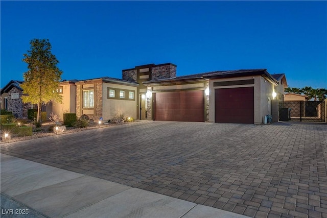 prairie-style house featuring a garage, fence, stucco siding, a gate, and decorative driveway