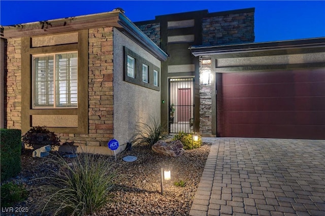 view of front facade with driveway, stucco siding, stone siding, and a garage