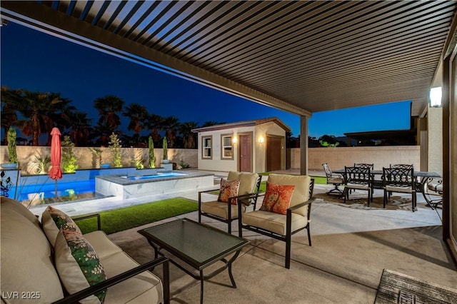 patio at night featuring outdoor dining space, a fenced backyard, an outdoor structure, and an outdoor hangout area