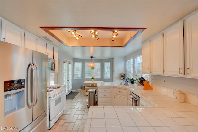 4517 Inez Dr, Las Vegas, NV 89130 - kitchen with stainless steel fridge with ice dispenser, white gas range oven, a raised ceiling, tile countertops, and a peninsula