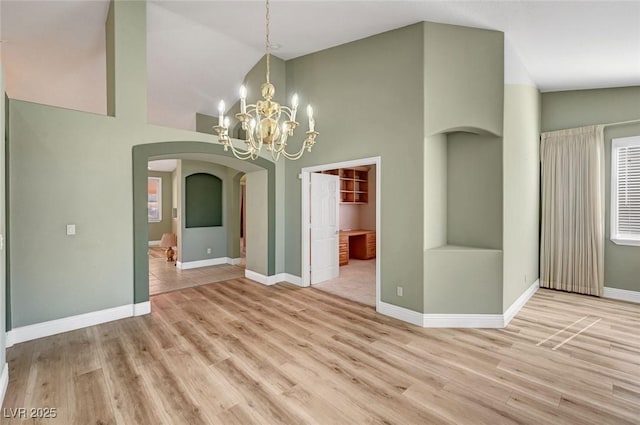 unfurnished dining area with a chandelier, arched walkways, baseboards, and wood finished floors