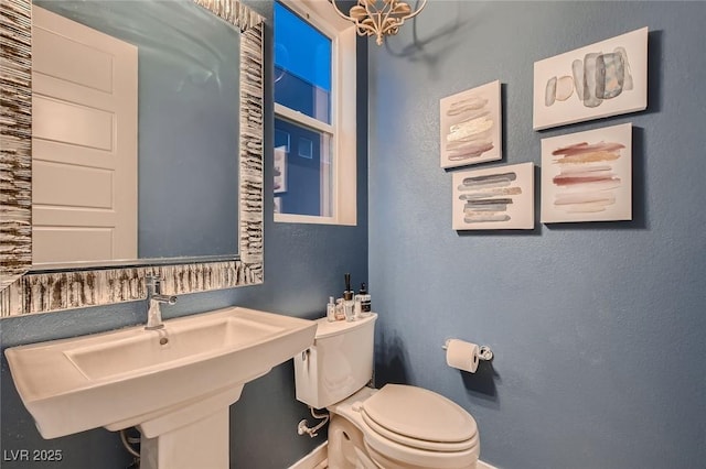 bathroom featuring a textured wall, toilet, a sink, baseboards, and a notable chandelier