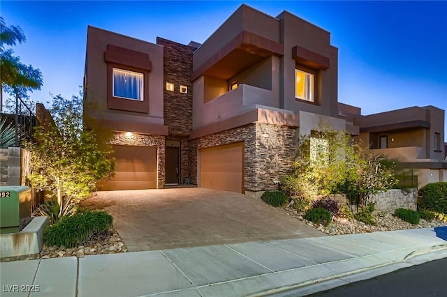 contemporary home with stone siding, a garage, decorative driveway, and stucco siding