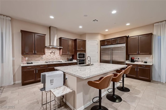 kitchen featuring a kitchen breakfast bar, visible vents, dark brown cabinetry, built in appliances, and wall chimney range hood