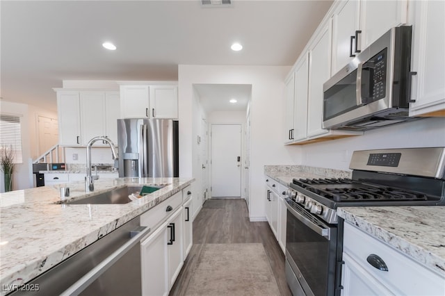 kitchen with appliances with stainless steel finishes, a sink, light stone counters, white cabinetry, and dark wood-type flooring