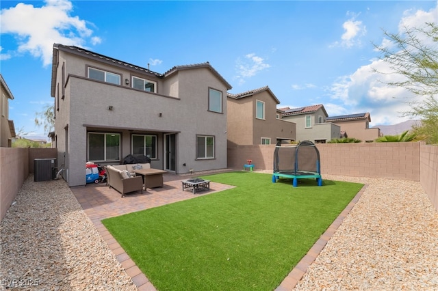 back of house with a lawn, a fenced backyard, a trampoline, and an outdoor living space with a fire pit