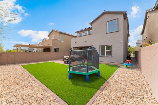 back of property with a fenced backyard, a trampoline, stucco siding, and a yard