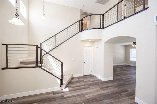 foyer entrance featuring arched walkways, a ceiling fan, a towering ceiling, wood finished floors, and stairs